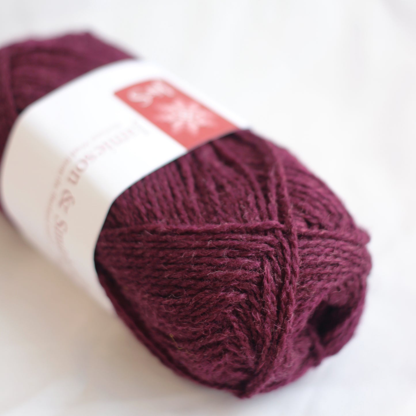 Ball of dark red yarn with a label on a white background