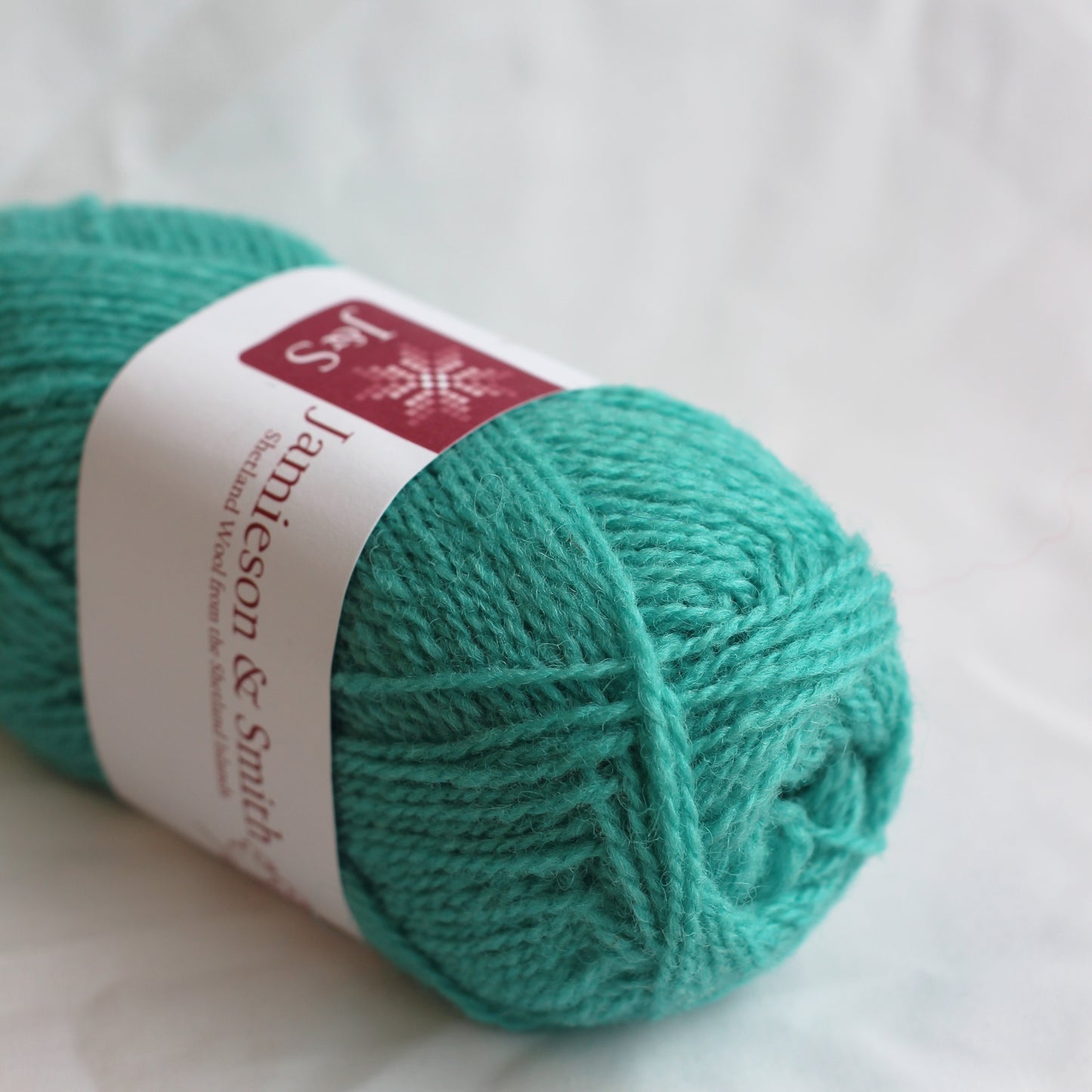 Turquoise yarn ball with a label on a white background